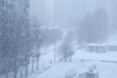 Urban landscape in blue colors with heavy snowfall on the street. Houses, people and roads in...