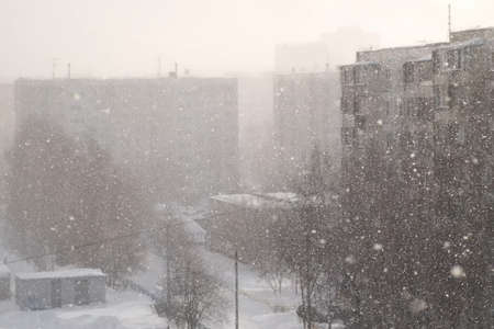 Urban landscape in blue colors with heavy snowfall on the street. Houses, people and roads in winter. Blizzard, snowstorm and big snowflakes falling from the sky. Cold freeze weather. Poor visibility.の写真素材
