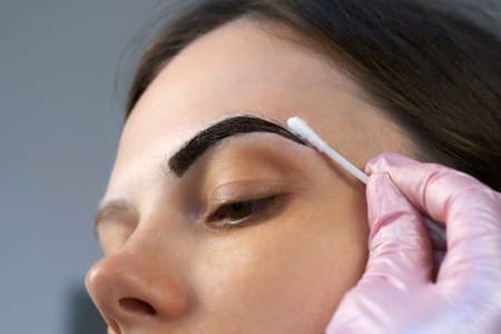 Cosmetologist is painting womans eyebrows in cosmetology clinic, closeup view. Aligns the contour...