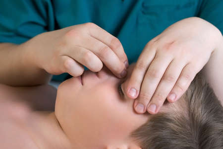 Session of craniosacral therapy, cure of teen boys nose by doctor therapist. Craniosacral therapist touches the boys nose and checks corrects of the nose by hands at hospital, side view of face.の写真素材