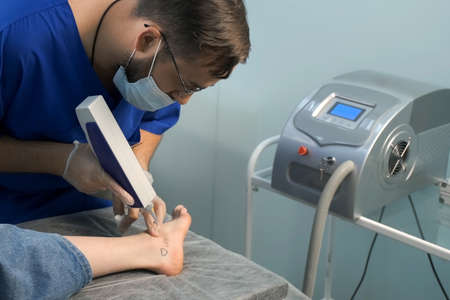 Laser removing of tattoo with words loser, lover and heart on womans foot in red and black colours, closeup hands of doctor in gloves. Romantic tattoo symbol of youth love and disappointment in life.の写真素材