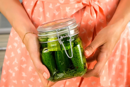 Woman holding glass jar with fresh pickles on kitchen at home, hands close-up. Cuisine, culinary, prepare cook dish, domestic food, recipe, fresh organic ingredients, products concept.の写真素材