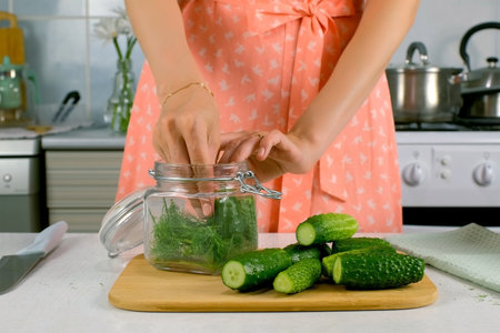Woman putting cucumbers in glass jar cooking pickles on kitchen, hands close-up, hands close-up. Cuisine, culinary, prepare cook dish, domestic food, recipe, fresh organic ingredients concept.の写真素材