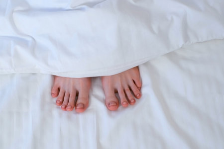 Woman's feet peek out from under the white linen; she is sleeping alone. Healthy sleep, relaxation,...