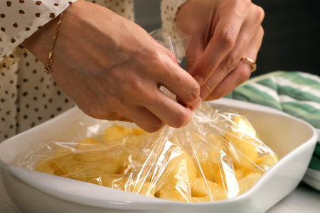 Woman putting apple pieces on ceramic baking sheet to bake in baking sleeve on kitchen, hands close-up. Housewife preparing homemade dish from apples. Culinary, cuisine healthy eating at home.の写真素材