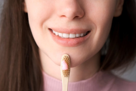 Smiling young brunette woman with organic bamboo toothbrush and toothpaste in her hands....