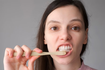 Smiling brunette woman with organic bamboo toothbrush and toothpasteis brushing her white teeth....