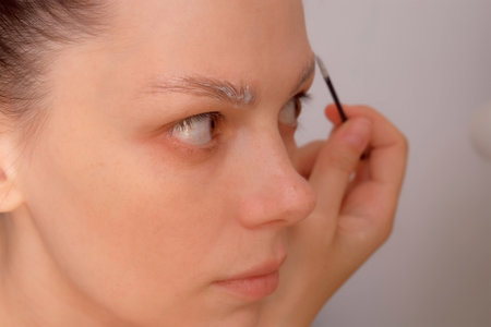 Middle aged brunette woman applying eyebrow fixation lamination cream gel looking at mirror....