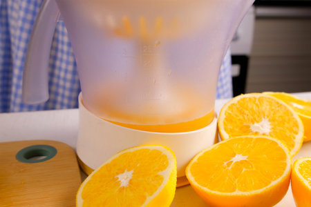 Woman chef squeezing oranges using electric juicer in kitchen at home. Healthy vegan ripe fruit...