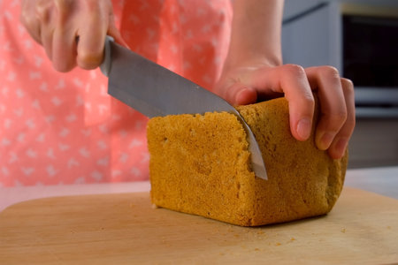 Woman hands cooking slicing loaf of bread on wooden cutting board. Female baker carefully slicing...