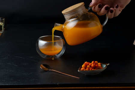 Pouring sea buckthorn juice into a glass cup on a black backgroundの写真素材