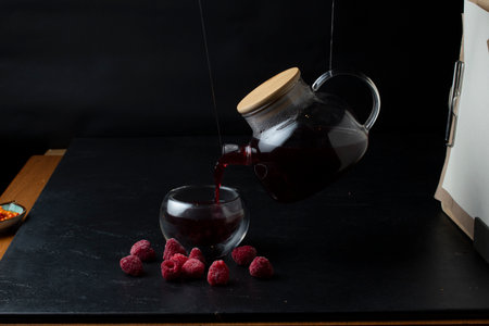 Pouring raspberry tea into a glass cup with raspberries on a black backgroundの写真素材