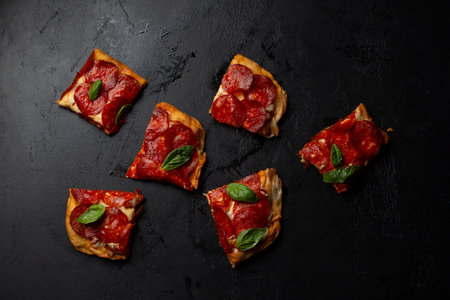 Slices of pizza with pepperoni and basil on black backgroundの写真素材