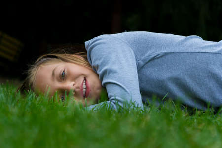 Young child girl lays aside in grass smiling with open mouthの写真素材