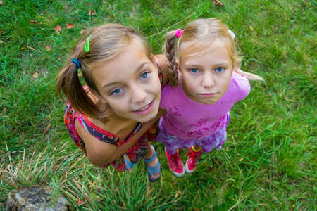 Smaller sister unhappy sad with happy older sister, children hug shot from above perspective