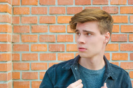 Unhappy sad teen boy with afraid expression on his face posing outdoor over red brick wall, side viewの写真素材