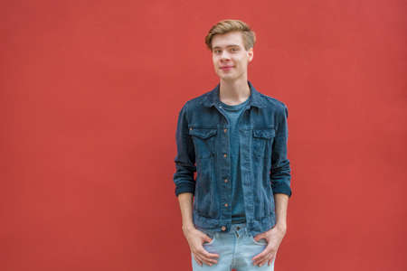 Teenager boy posing over red contrasting background wall standing casual with hands in pocketsの写真素材