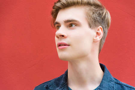 Clouseup portratit of teen boy looking away to the side happy posing over red contrasting backgroundの写真素材