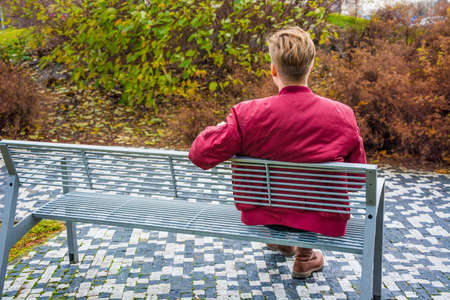 Young teen boy on date waiting for his girlfriend on valentine outdoor on park bench, sitting sad...