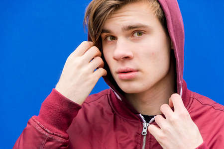 Teenager boy closeup face in hood over contrasting blue backgroundの写真素材