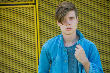 Closeup portrait of teenage boy in blue denim with hair covering his eye and face, modern fashion pose over yellow contrast urban backgroundの写真素材