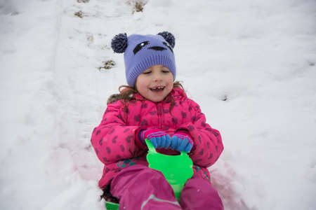 Little girl sliding on snow in winter havin fun playing outdoor