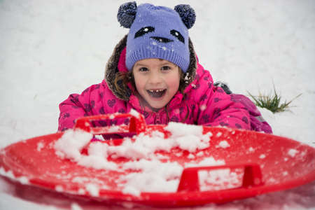 Excited happy child sliding on snow playing outside in winter smiling and having funの写真素材