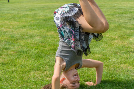 Young child girl standing on her head in garden doing gymnatic and having fun