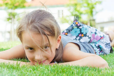 Happy child girl in dress lays in grass at city park enjoing sun and summer holidayの写真素材