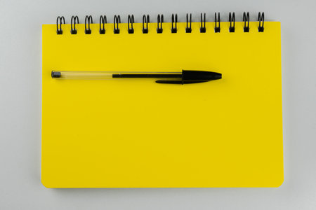 Yellow note book with black pen on white background. Top views.の写真素材