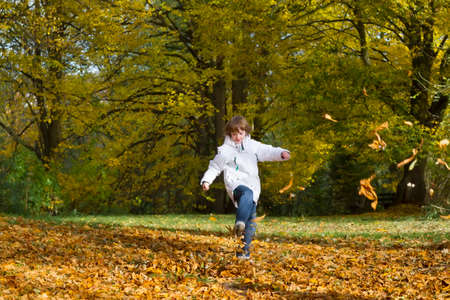 Boy jumping and playing with golden autumn leaves の写真素材