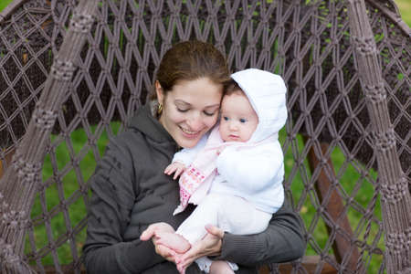 Attractive young mother playing with baby feet sitting in a hammock 