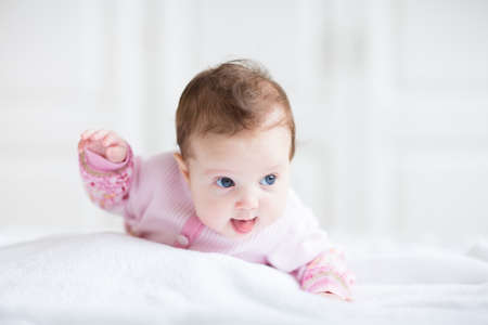Cute funny baby girl in a pink cardigan trying to crawl の写真素材