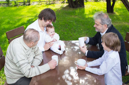 Four generations of one family sitting at a wooden table in the garden drinking coffee and tea 