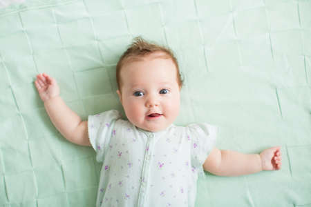 Beautiful baby girl with blue eyes playing on a knitted mint blanket 