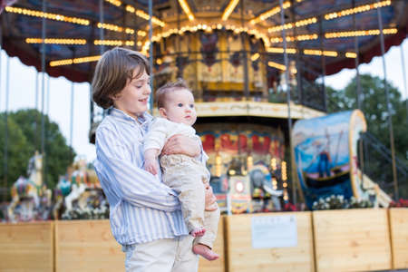 Cute boy and his baby sister standing in front of a carousel の写真素材