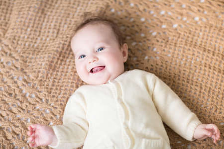 Laughing happy baby in a warm cardigan on a handmade knitted blanket 