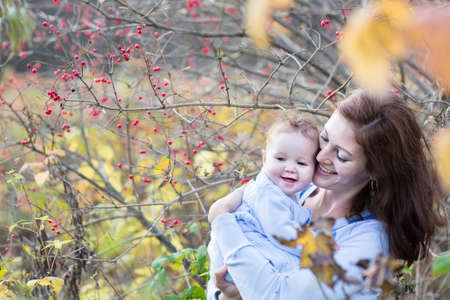 Happy young mother hugging her baby under an ashberry bush の写真素材