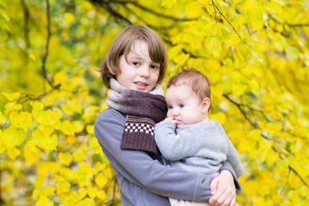 Portrait of brother and baby sister with a colorful yellow leaves background の写真素材