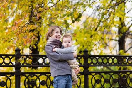 Boy holding his sister walking in an autumn park with colorful trees の写真素材
