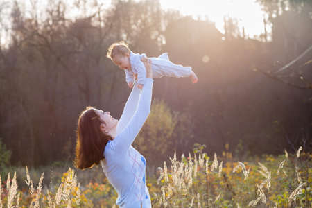 Young mother holding her little baby on a sunny day in a meadow の写真素材