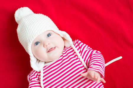 Sweet baby girl in a warm white hat on red background の写真素材