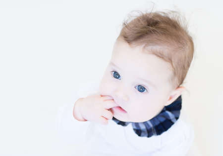 Little baby girl in a white shirt with plaid blue collar sucking on her finger の写真素材