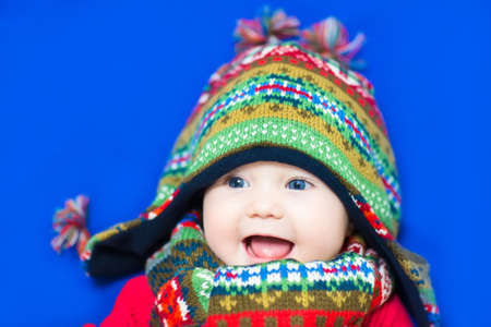 Funny baby in a colorful knitted hat on blue background の写真素材