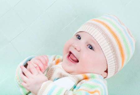 Playing baby girl on a green blanket wearing knitted sweater and hat の写真素材