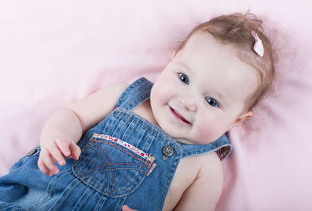 Cute little baby girl in a jeans dress on a pink blanket の写真素材