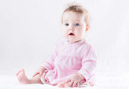 Beautiful baby girl in a pink dress on a white background の写真素材