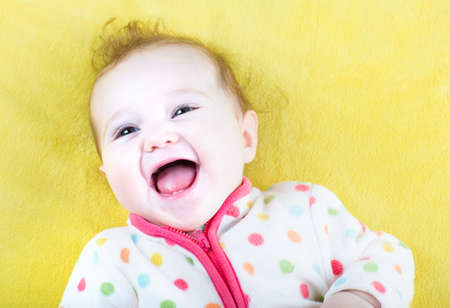 Funny laughing baby in a colorful sweater on yellow blanket の写真素材