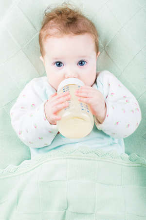 Beautiful little baby with a milk bottle under a warm knitted blanket の写真素材