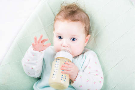 Adorable baby girl on a green knitted blanket drinking milk の写真素材